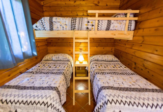 Accogliente stanza in bungalow di legno con tre letti singoli e un letto a castello, illuminata da una lampada centrale.