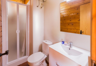 Bagno moderno con doccia, WC, lavabo bianco e legno presso La Llosa Mestral Bungalows in Spagna.