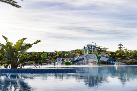 Area giochi d’acqua vicino alla piscina di La Llosa Mestral-BUNGALOWS-G in Spagna, con scivoli e piante verdi.