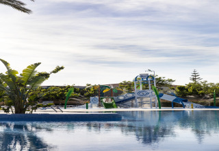 Area giochi d’acqua vicino alla piscina di La Llosa Mestral-BUNGALOWS-G in Spagna, con scivoli e piante verdi.