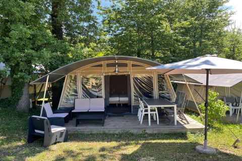Tienda safari en Camping Le Clou 1 en Francia con zona de asientos al aire libre y sombrilla entre árboles.