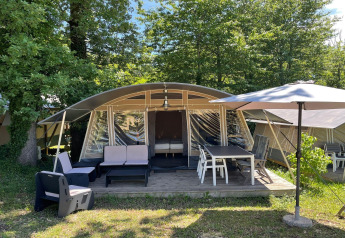 Tienda safari en Camping Le Clou 1 en Francia con zona de asientos al aire libre y sombrilla entre árboles.