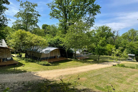 Tiendas safari en Camping Le Clou 1 en Francia, rodeadas de árboles verdes y cielo azul soleado.