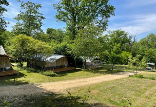 Tiendas safari en Camping Le Clou 1 en Francia, rodeadas de árboles verdes y cielo azul soleado.
