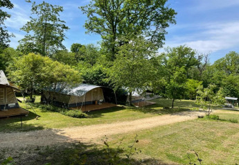 Tiendas safari en Camping Le Clou 1 en Francia, rodeadas de árboles verdes y cielo azul soleado.