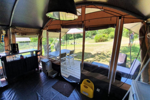 Interior de una tienda safari en Camping Le Clou 1 en Francia con zona comedor, sillas y vista al jardín.