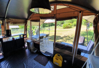 Interior de una tienda safari en Camping Le Clou 1 en Francia con zona comedor, sillas y vista al jardín.