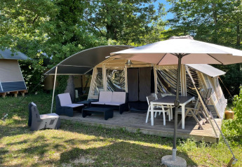 Tienda safari en Camping Le Clou 1 en Francia, con salón exterior, mesa de comedor y sombrilla en la terraza.