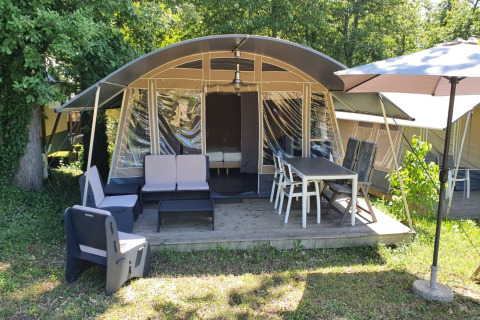 Tienda safari en Camping Le Clou 1 con terraza amueblada, mesa exterior, sillas y sombrilla grande.