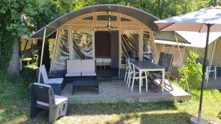 Safaritent bij Camping Le Clou 1 met een gemeubileerd terras, stoelen, tafel en grote parasol buiten.