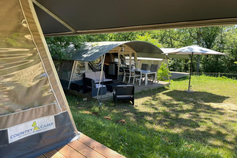 Tienda safari Camping Le Clou 1 en Francia con terraza exterior, sillas y sombrilla entre naturaleza.