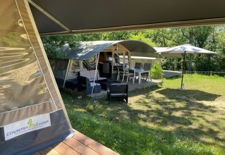 Tienda safari Camping Le Clou 1 en Francia con terraza exterior, sillas y sombrilla entre naturaleza.