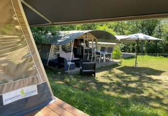 Tienda safari Camping Le Clou 1 en Francia con terraza exterior, sillas y sombrilla entre naturaleza.