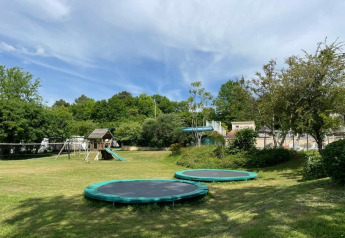 Parque infantil con dos camas elásticas, tobogán y columpios en Camping Le Clou 1, Francia.