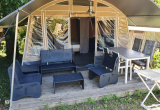 Terraza de tienda safari en Camping Le Clou 1, Francia, con muebles exteriores y mesa para comer.