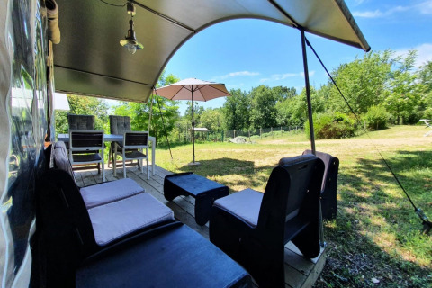 Zona de estar al aire libre en la tienda safari Camping Le Clou 1 en Francia, con sillas y sombrilla.