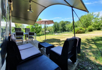 Zona de estar al aire libre en la tienda safari Camping Le Clou 1 en Francia, con sillas y sombrilla.