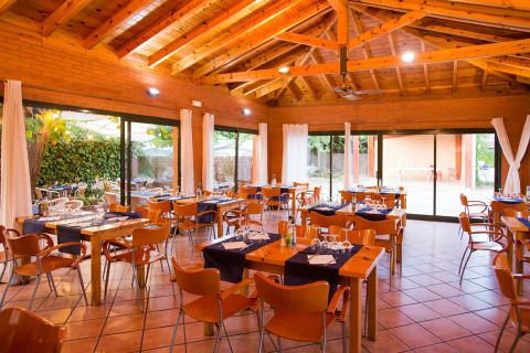 Sala da pranzo con interni in legno a La Llosa Mestral-BUNGALOWS-G in Spagna, tavoli apparecchiati e vista giardino.