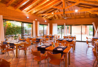 Sala da pranzo con interni in legno a La Llosa Mestral-BUNGALOWS-G in Spagna, tavoli apparecchiati e vista giardino.
