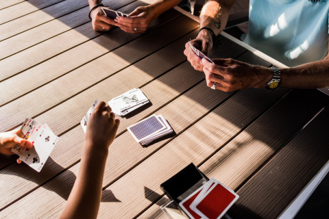 Mensen spelen een kaartspel aan een houten tafel in een safaritent, zonlicht schijnt naar binnen.
