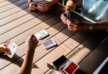 Personas jugando a las cartas sobre una mesa de madera en una tienda safari, con luz solar entrando.