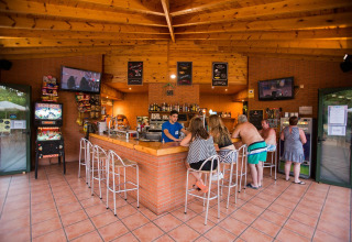 Zona bar interna di La Llosa Mestral BUNGALOWS-G in Spagna con clienti, sgabelli, macchinette e televisori.