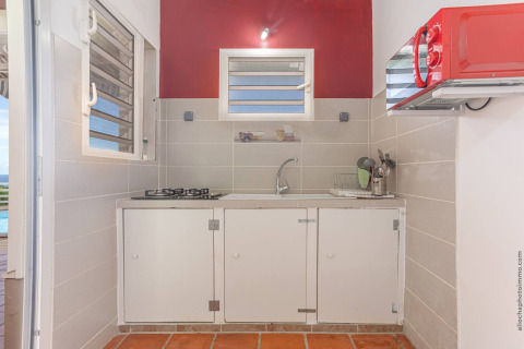 Pequeña cocina glamping con estufa de gas, fregadero, microondas rojo y azulejos claros, vista exterior.