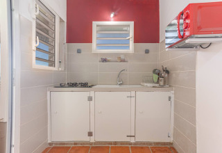 Pequeña cocina glamping con estufa de gas, fregadero, microondas rojo y azulejos claros, vista exterior.