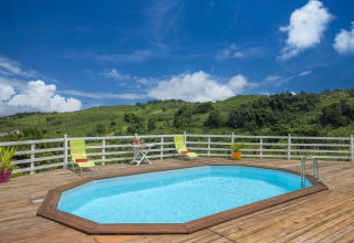 Piscina octogonal sobre tarima de madera con tumbonas y vistas al campo verde bajo un cielo azul despejado.
