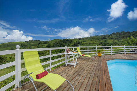 Terraza junto a la piscina con tumbonas y mesa, rodeada de verdes colinas bajo un cielo azul en Portugal.