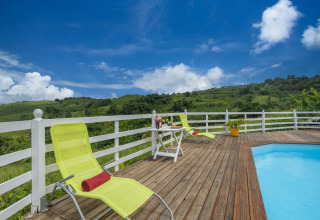 Terraza junto a la piscina con tumbonas y mesa, rodeada de verdes colinas bajo un cielo azul en Portugal.