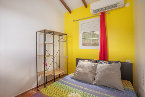 Dormitorio luminoso con pared amarilla, cama, armario abierto y aire acondicionado en bungalow con piscina en Portugal.