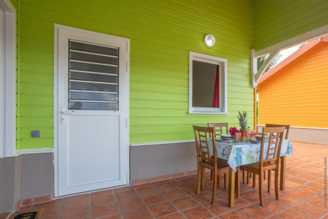 Zona de comedor exterior en un bungalow verde lima con mesa y sillas de madera en Portugal.