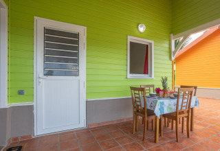 Zona de comedor exterior en un bungalow verde lima con mesa y sillas de madera en Portugal.