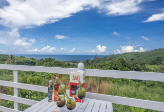 Bebidas sobre una mesa en un alojamiento glamping con vistas a colinas verdes y al mar azul.