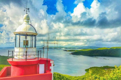 Faro junto a la costa con colinas verdes y mar, visto desde un alojamiento glamping panorámico.