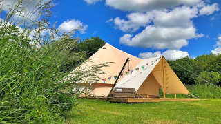 Bulrush Bell Teepee tent set up on a grassy field under a blue sky with some fluffy white clouds.