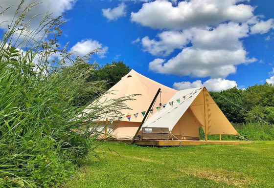 Bulrush Bell Teepee tent set up on a grassy field under a blue sky with some fluffy white clouds.