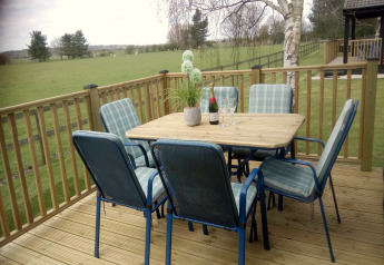 Terrasse en bois du lodge New Puddledock au Royaume-Uni avec table, chaises, vin et vue champêtre.