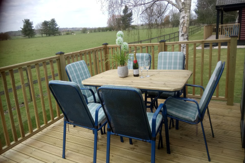 Træterrasse ved New Puddledock-lodgen i Storbritannien med bord, stole, vin og udsigt til mark.