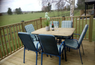 Træterrasse ved New Puddledock-lodgen i Storbritannien med bord, stole, vin og udsigt til mark.