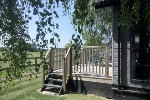Solbeskinnet udsigt til træterrasse og græsplæne ved New Puddledock Lodge i Storbritannien, omgivet af grønne marker.