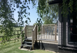 Solbeskinnet udsigt til træterrasse og græsplæne ved New Puddledock Lodge i Storbritannien, omgivet af grønne marker.