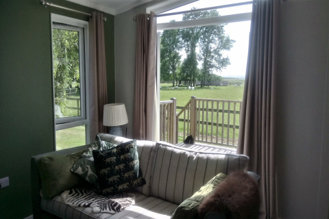 Stue i New Puddledock lodge, UK, med udsigt over græsplæne og træer gennem store vinduer.