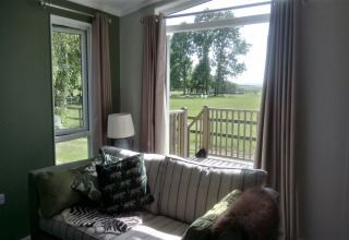 Stue i New Puddledock lodge, UK, med udsigt over græsplæne og træer gennem store vinduer.
