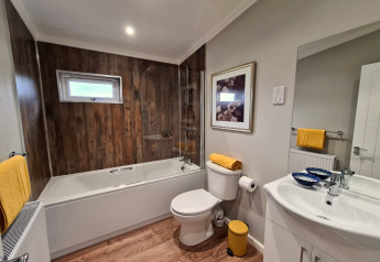 Salle de bain moderne au lodge New Puddledock, Royaume-Uni, avec bois, baignoire et accents jaunes.