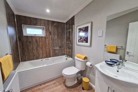 Moderne badeværelse i New Puddledock-lodge, UK, med trægulv, badekar og gule detaljer.
