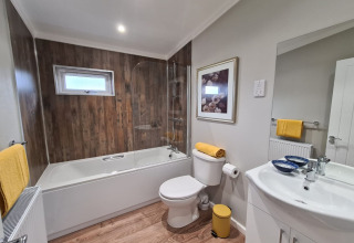 Moderne badeværelse i New Puddledock-lodge, UK, med trægulv, badekar og gule detaljer.