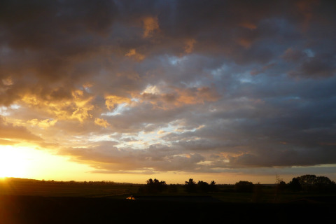 Solnedgang over marker ved New Puddledock Lodge i Storbritannien, med dramatiske skyer og gyldent lys.