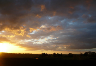 Solnedgang over marker ved New Puddledock Lodge i Storbritannien, med dramatiske skyer og gyldent lys.